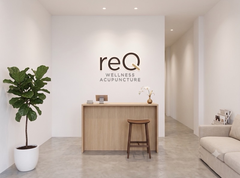 美容鍼 reQの受付イメージ。白い壁にreQのロゴ、木のカウンター、観葉植物のある静かな空間